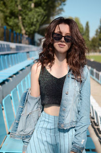 Portrait of young woman wearing sunglasses while standing against swimming pool