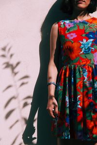 Midsection of woman wearing floral patterned dress standing against wall during sunny day