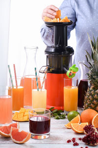 A woman prepares citrus juices from orange, grapefruit, pomegranate, pineapple, mango on a juicer.