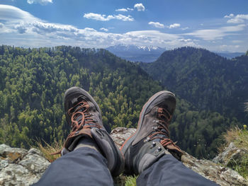 Low section of person relaxing on mountain against sky