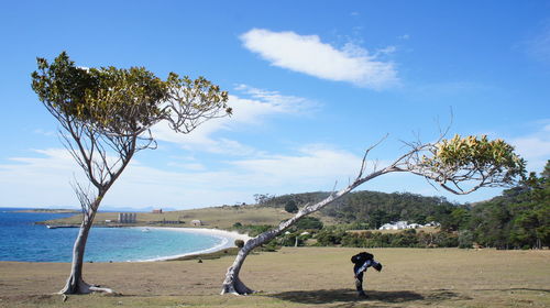 Side view of man bending by tree on field against sky