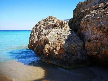 Rocks in sea against clear blue sky