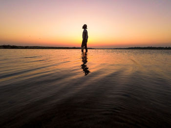 Man standing in sea against sky during sunset