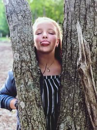 Teenage girl sticking out tongue while standing by tree trunk