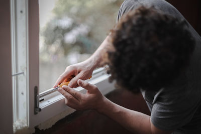 Caucasian man cleans a window frame with a construction knife.