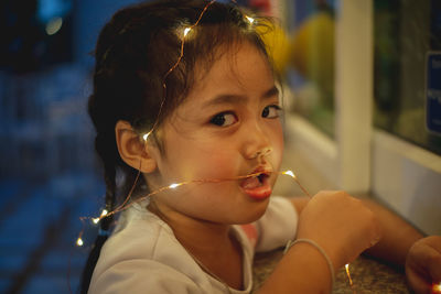 Close-up portrait of cute girl with mouth open holding illuminated lights