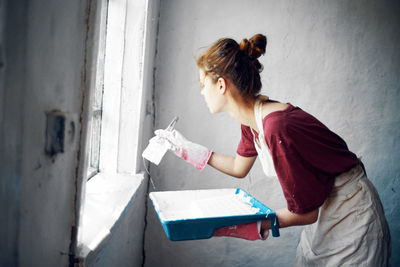 Side view of woman standing against wall at home