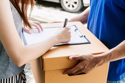 Midsection of woman signing paper while delivery person holds package