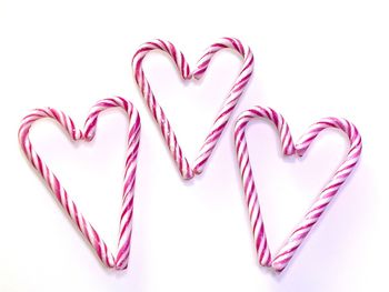 High angle view of candy canes arranged in heart shapes on white background