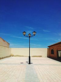 Street light on footpath by building against blue sky