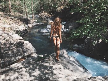 Woman standing on rock against waterfall in forest