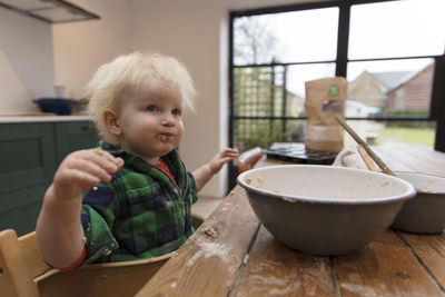 Cute baby sitting by food on table at home