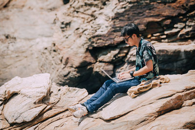 Man using laptop while sitting on rock