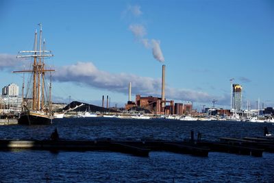 Smoke emitting from industry by sea against sky