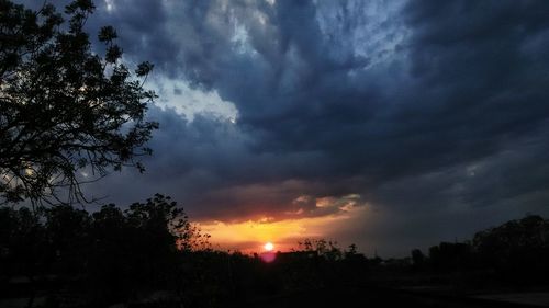 Silhouette trees against dramatic sky during sunset
