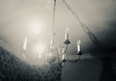 Low angle view of illuminated light bulb hanging on wall