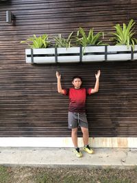 Full length portrait of happy young man standing against brick wall