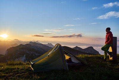 Full length of man looking at view while camping on field against sky during sunset