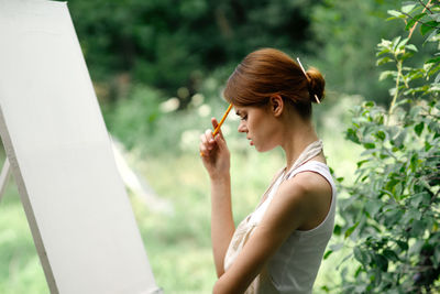 Side view of young woman holding plant