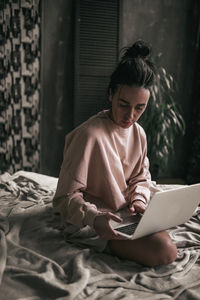 Woman using mobile phone while sitting on bed at home