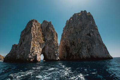 Rock formations in sea against clear blue sky