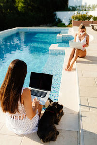 Women using laptop sitting by pool