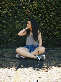 Young woman sitting on cobbled street against plants