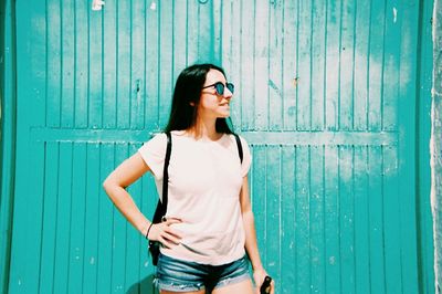 Smiling young woman with hand on hip standing against wooden wall