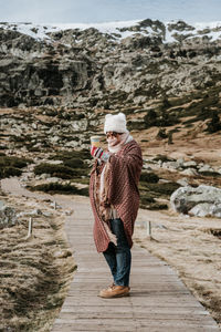 Woman wearing knit hat standing on footpath against field