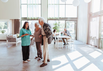 Full length of nurse showing digital tablet to senior couple at nursing home