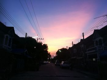 Cars on street amidst buildings against sky at sunset