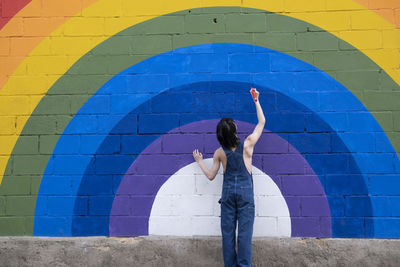 Young man drawing with pencil on rainbow mural