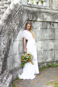 Bride holding bouquet while standing against wall