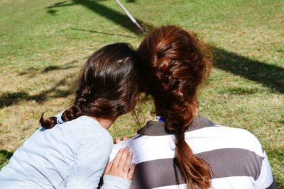 Rear view of mother and daughter with braided hair sitting on field at park