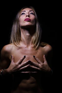 Young woman covering breast while standing against black background