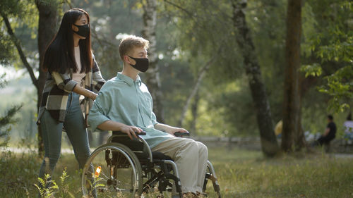 Young woman wearing mask with handicapped boyfriend at park