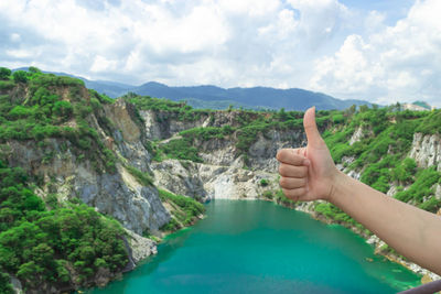 Cropped hand of woman gesturing thumbs up against landscape