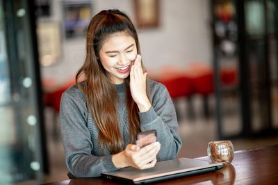 Smiling woman using mobile phone while sitting in cafe