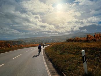 Rear view of cyclist cycling on road against landscape