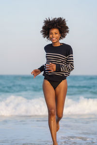 Woman with afro hair having fun at the beach running from the waves