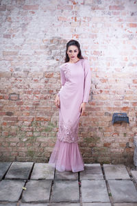 Portrait of young woman standing against pink brick wall