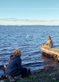 Rear view of couple sitting on sea shore against sky