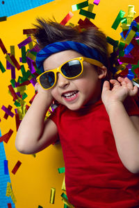 Child a boy in a red t shirt and sunglasses is lying on yellow paper resting at home