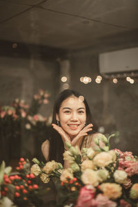 Portrait of smiling young woman by flowers at home