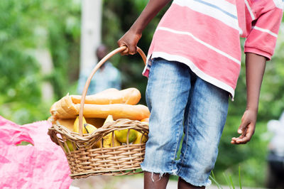 Child holding a basket of food containing fruit and bread.