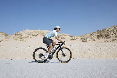 Mature cyclist riding bicycle on road by sand dunes