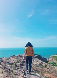 Rear view of woman walking on rock over sea against sky