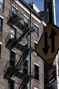 Low angle view of road sign against building with fire escape