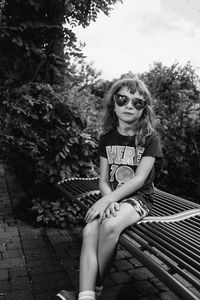Portrait of cute girl wearing heart shape sunglasses sitting against trees