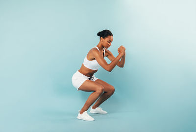 Full length of woman exercising against blue background